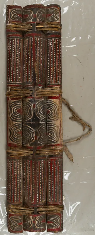 Three decorated split logs fastened together into a shield with rattan.