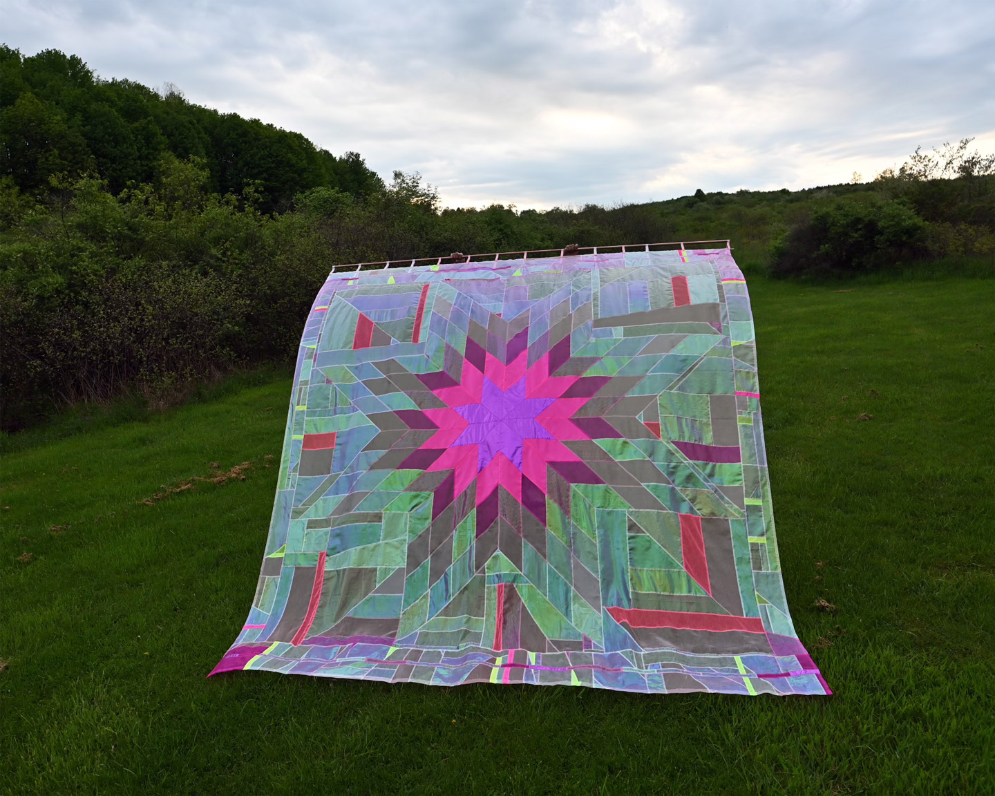 A translucent quilt with a star design, being held aloft in a green field.