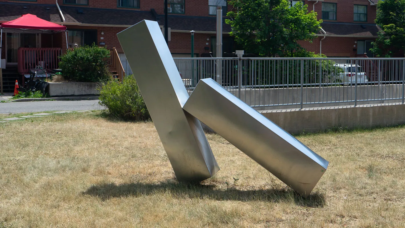 Two stainless steel beams leaning on each other in a grassed courtyard.