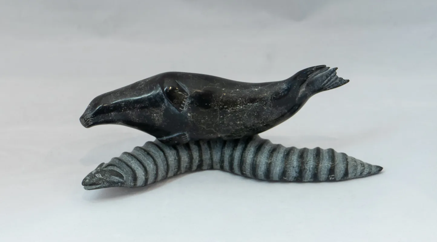 Seal in black stone balanced on large worm in green stone. 