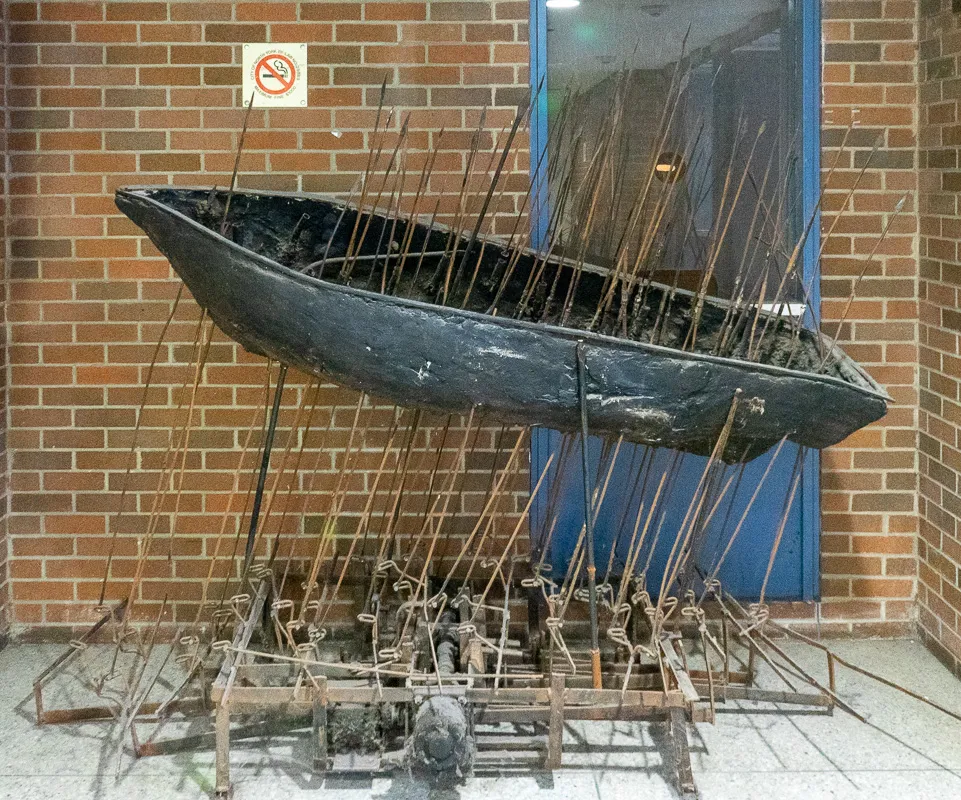 A simple boat supported by a raft of spears. The sculpture is on a mechanized base.