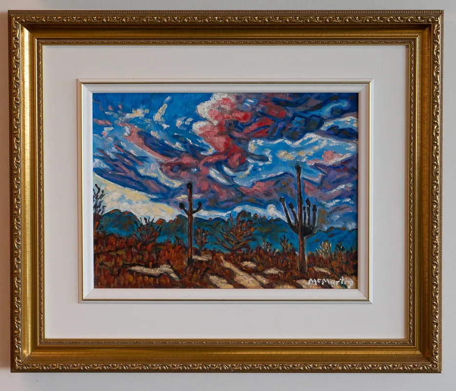 Mountainous desertscape in blue and red. Some cactus in the middle ground.