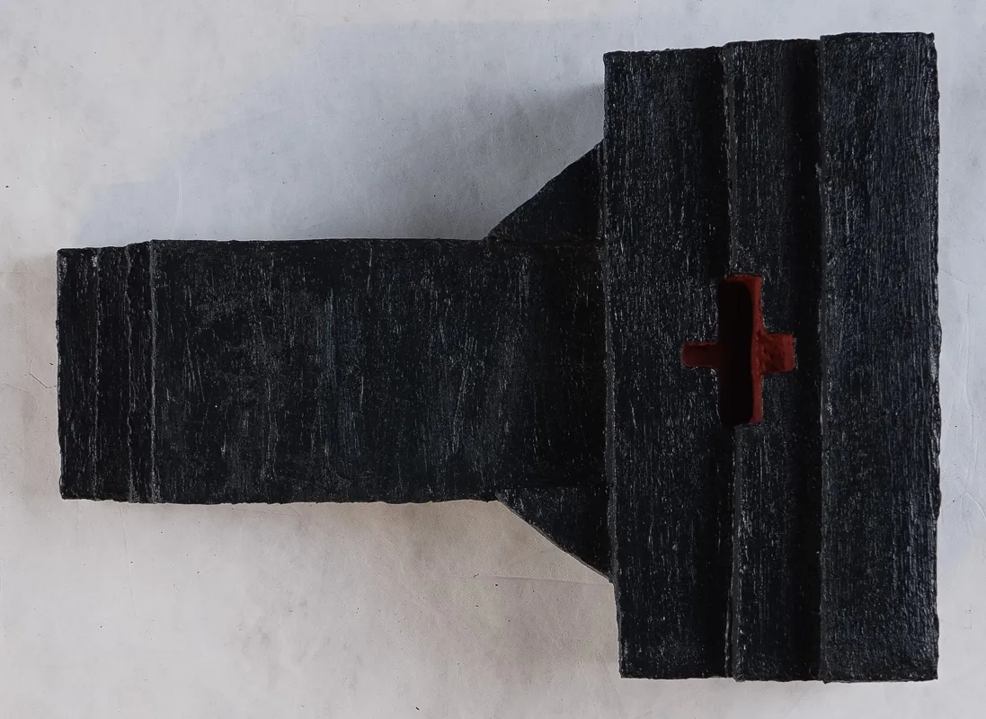 A blocky wooden sculpture in black with a vague look of a vacuum attachment.