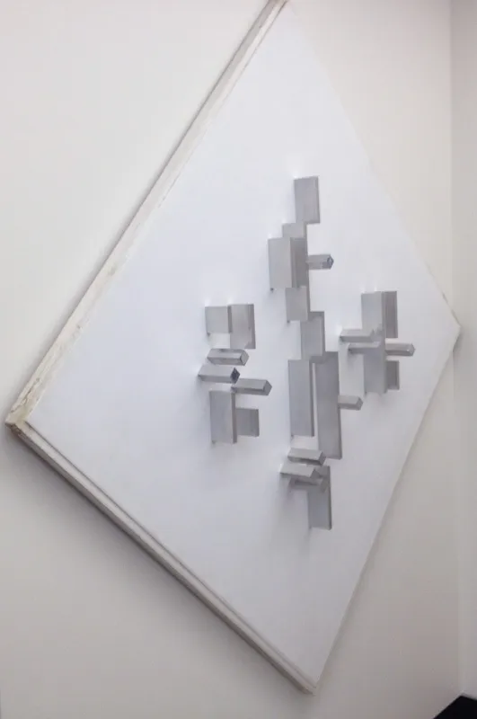 White square support at a 45 degree angle with aluminum cuboids arrayed in the centre.