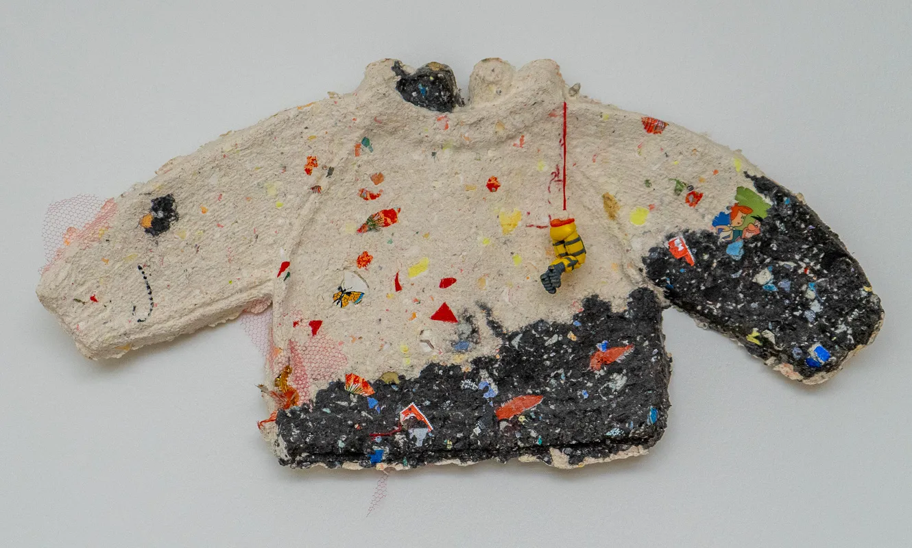 A sweater in white with red blotches with the waistband and half of one arm in black.