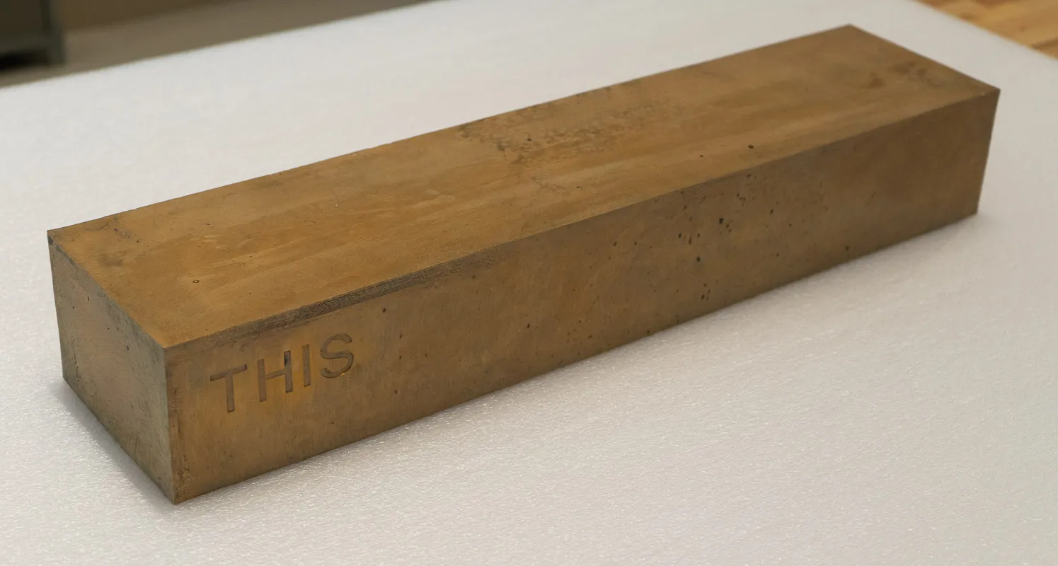 Bronze box with text debossed in side reading, on one side "Touch" upside down and on the other side "This" right side up. Bronze is patined with touch. 