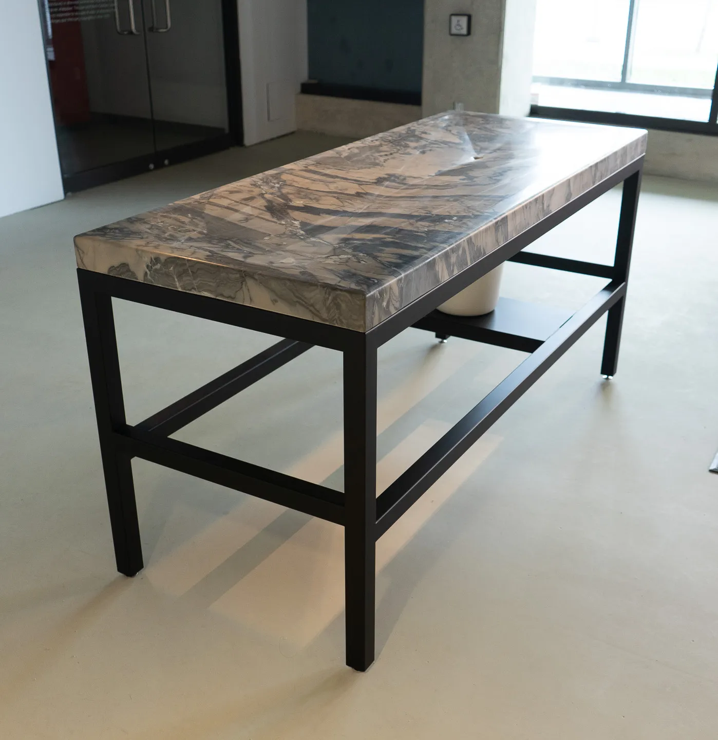 A stylized mortuary table with marble top and bucket under drain hole.