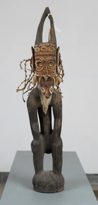 Wooden human figure with shell and rope adornments. 