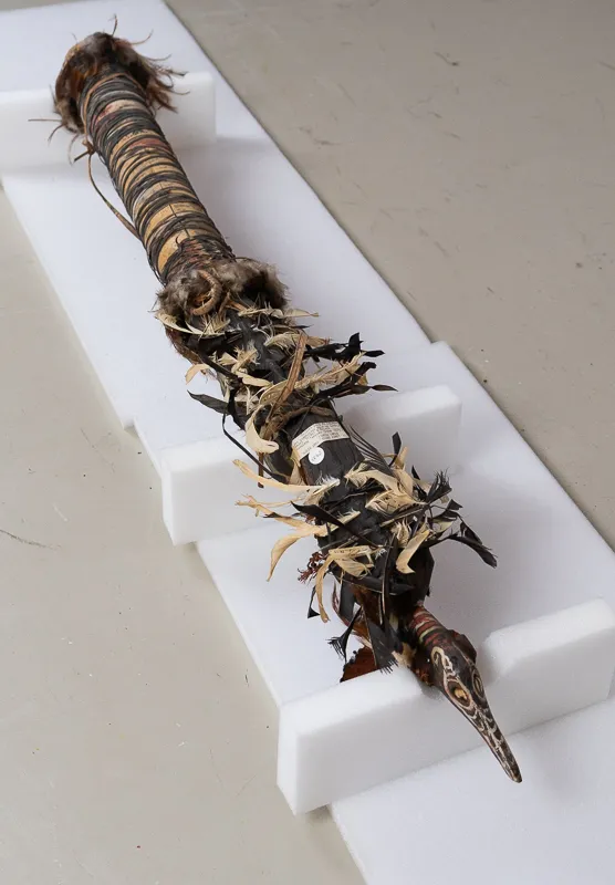 Ornate large wooden flute decorated with bird motifs, feathers, and sundry.
