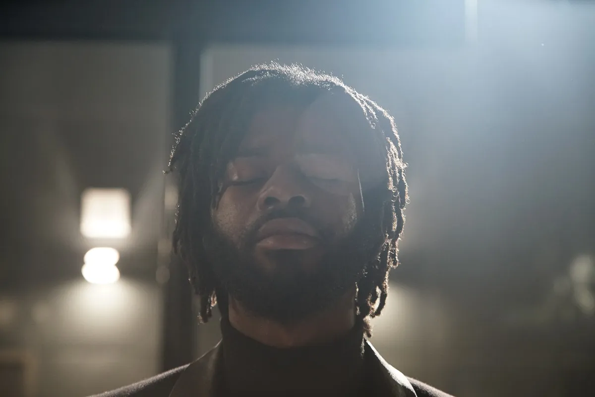 Close-up portrait of a young bearded Black man, surrounded by lens flare that appears like fog. 